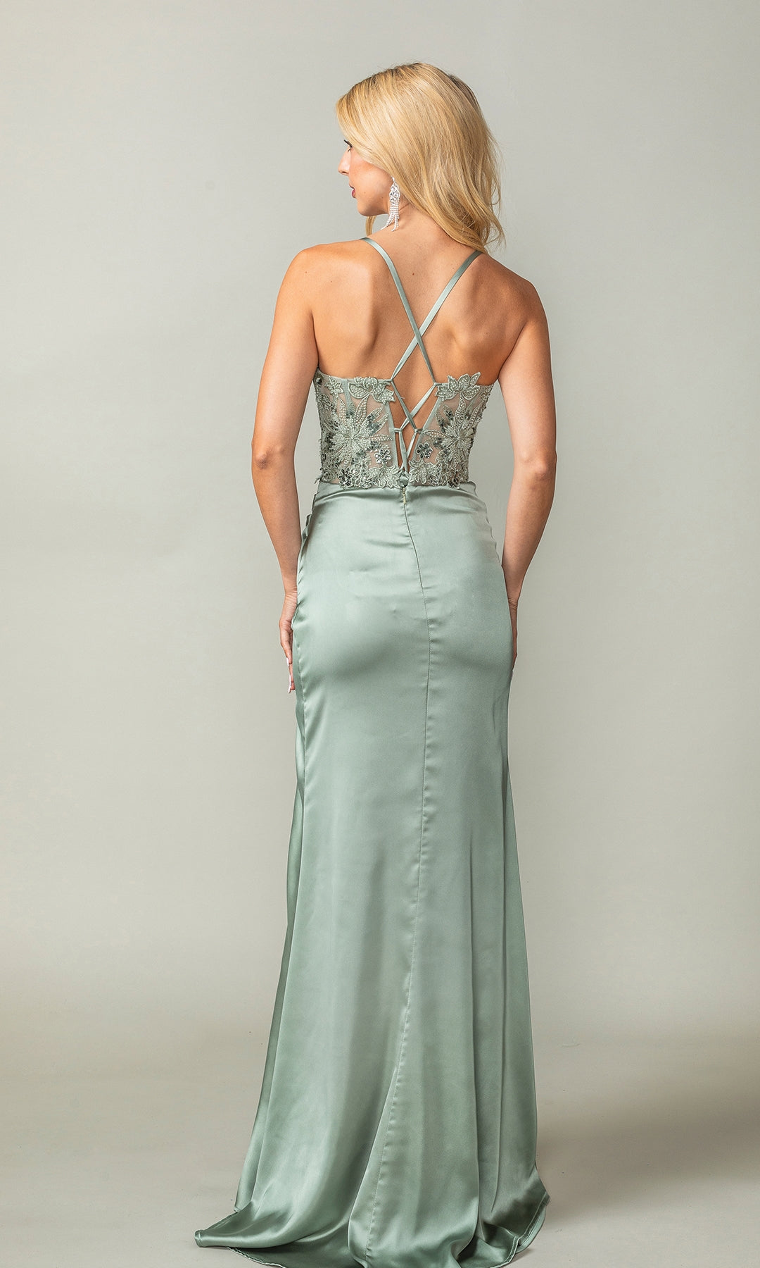 A woman, facing away from the camera against a plain backdrop, wears the Sheer-Waist Long Prom Dress: Dancing Queen 4416—a light green satin gown with crisscross straps and lace bodice detailing.